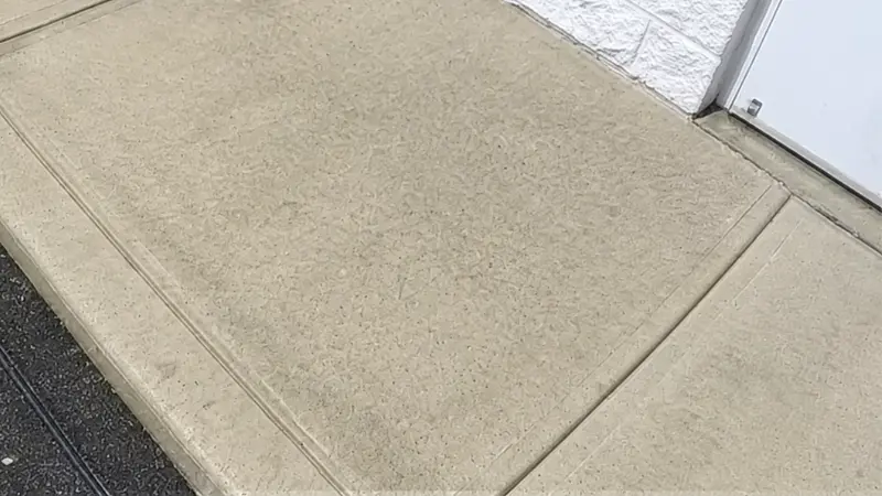 Clean concrete entry pad and walkway by a white door