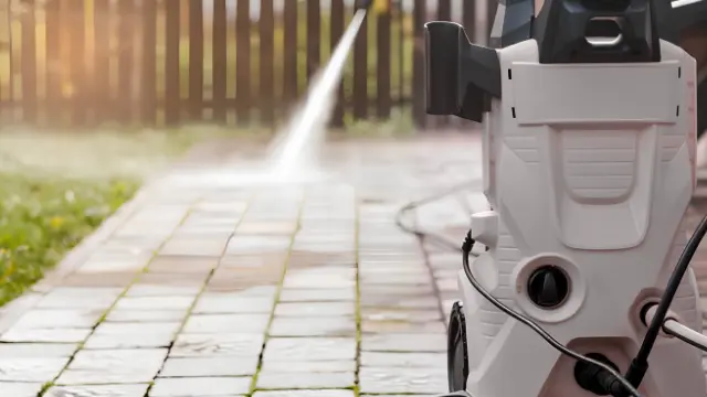 Pressure washer spraying a paver walkway clean in front of a wooden fence.