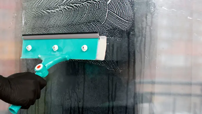 Pressure Washing in Wilmington Gloved hand using a teal squeegee to wipe soapy water off glass during window cleaning.
