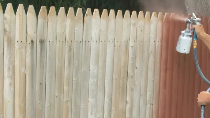Wood Fence Stain Spraying - Professional Pressure Washing Wilmington, NC Spray gun applying reddish stain to a wood picket fence - Professional Pressure Washing Wilmington, NC